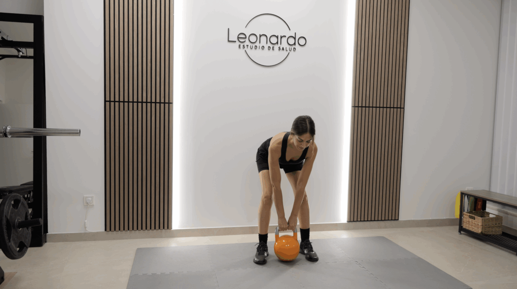 Paciente realizando un ejercicio de peso muerto con kettlebell durante una sesión de readaptación física en el gimnasio de la clínica.
